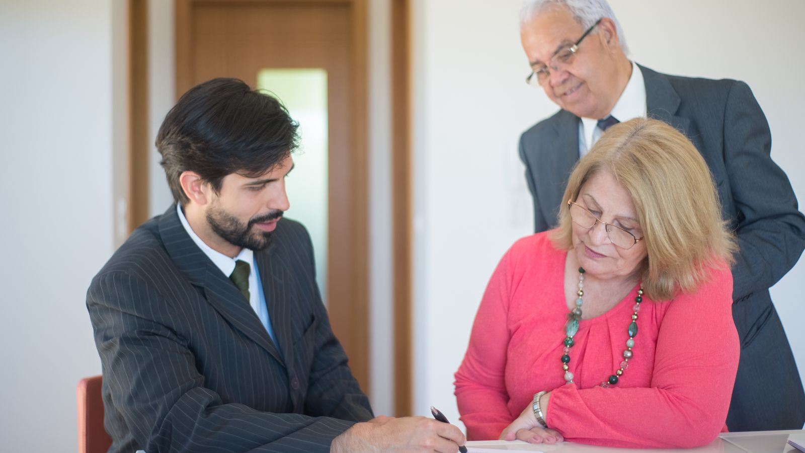 Couple âgé signant des documents immobiliers avec une conseillère autour d'une table