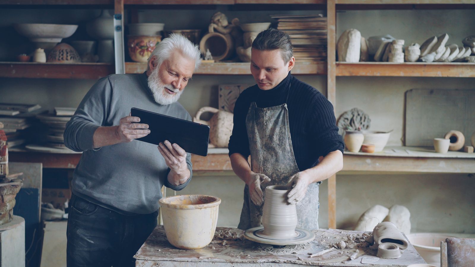Homme âgé transmettant un geste de poterie dans un atelier collectif
