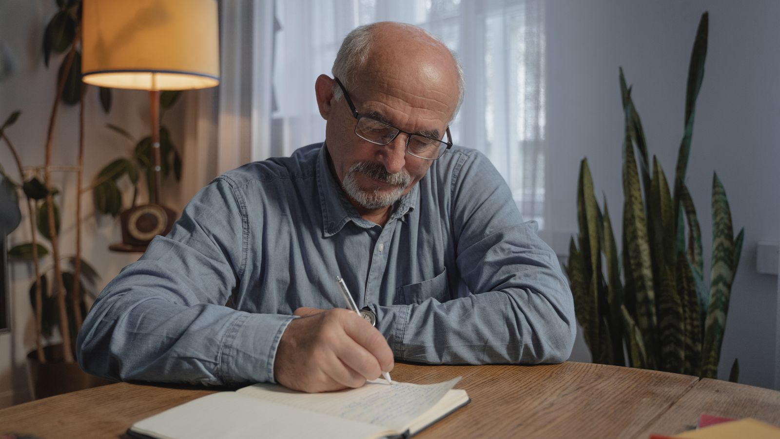 Homme âgé écrivant dans un carnet à son bureau avec des documents à portée de main