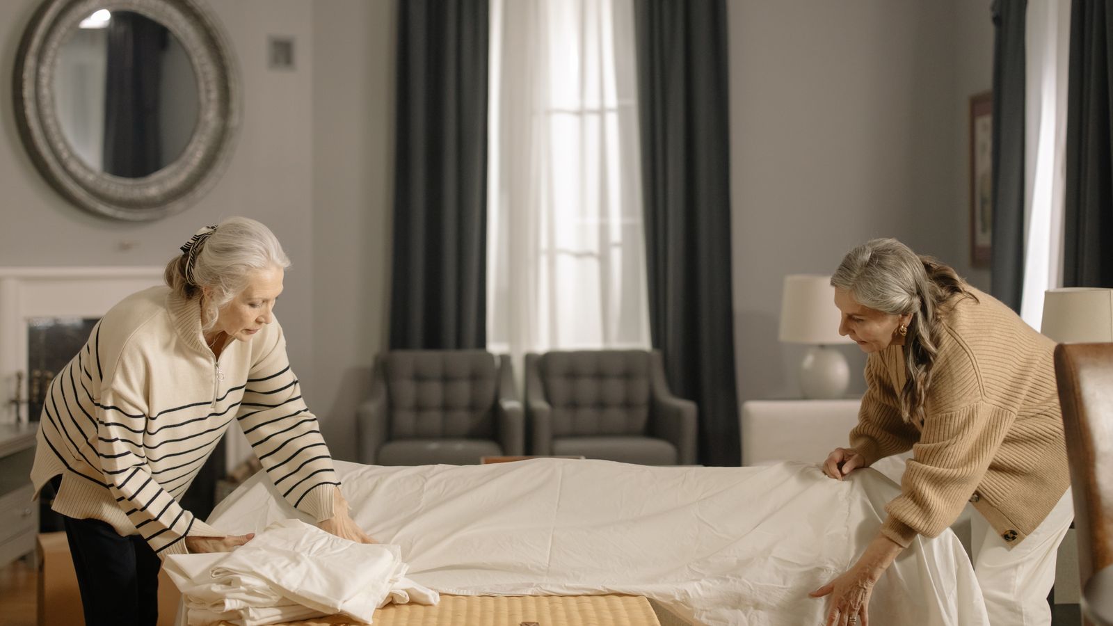 Deux femmes préparant une chambre lumineuse avec des draps pliés