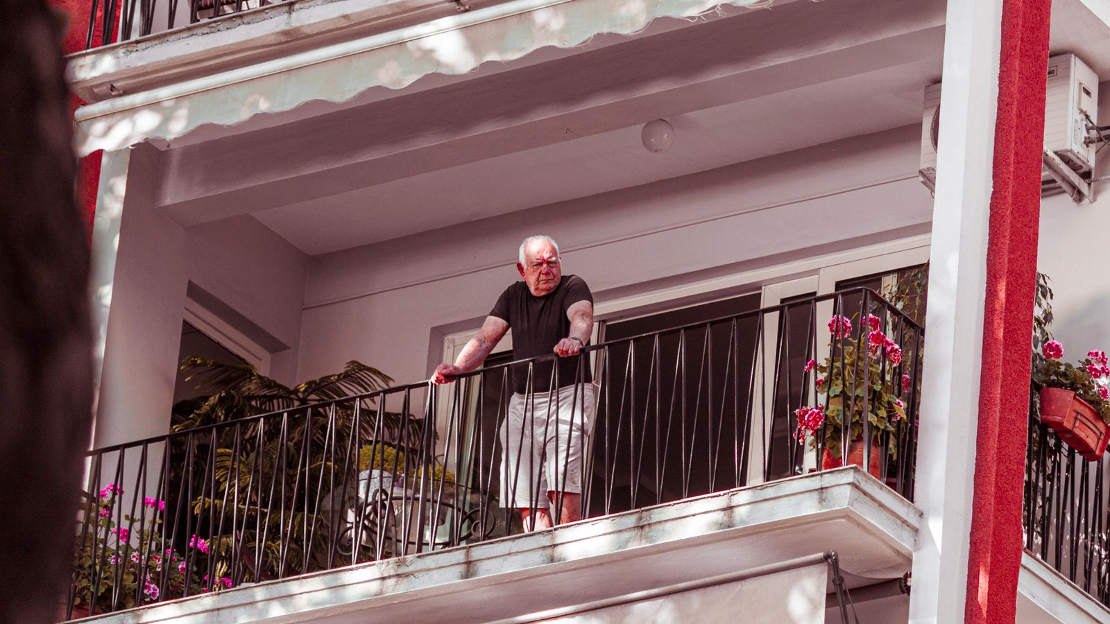 Homme âgé debout sur un balcon entouré de plantes au soleil