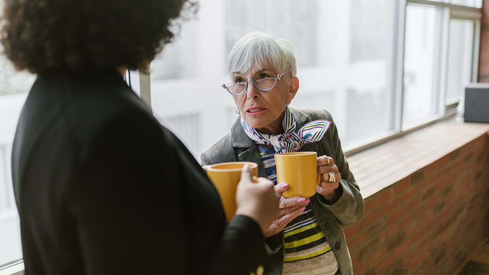 Femme expérimentée échangeant avec une collègue autour de deux cafés au bureau