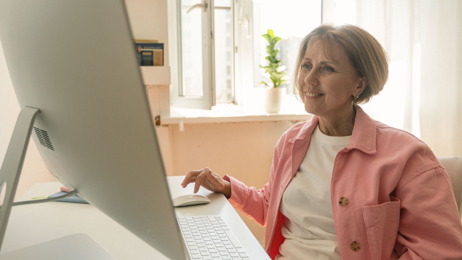 Femme aux cheveux blancs utilisant un ordinateur à son bureau chez elle