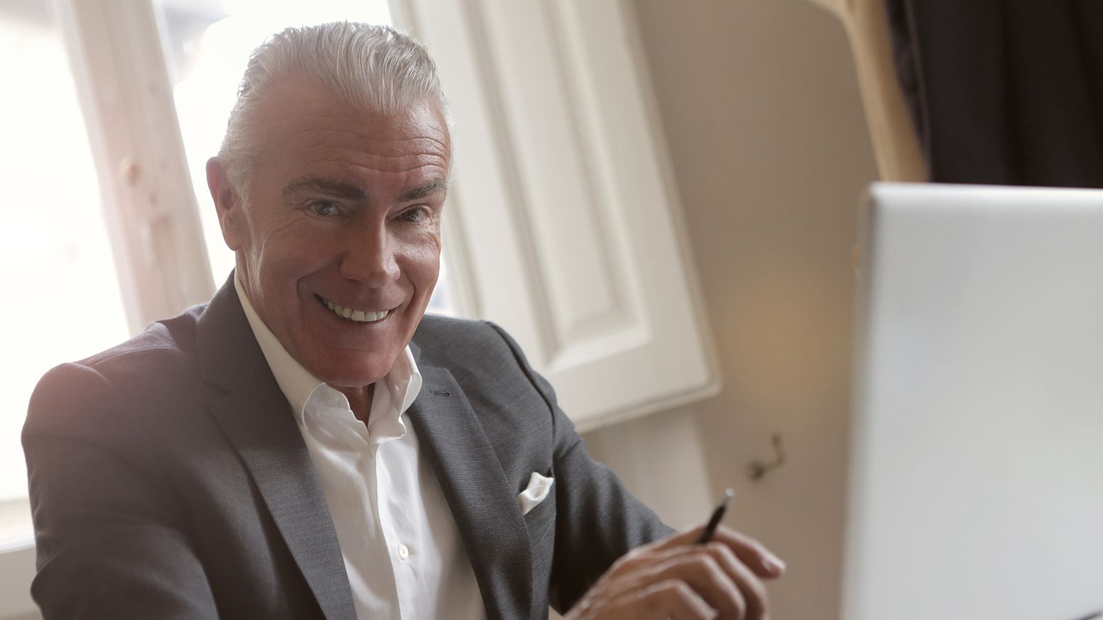 Homme de plus de 60 ans travaillant sur ordinateur avec un carnet dans un bureau lumineux